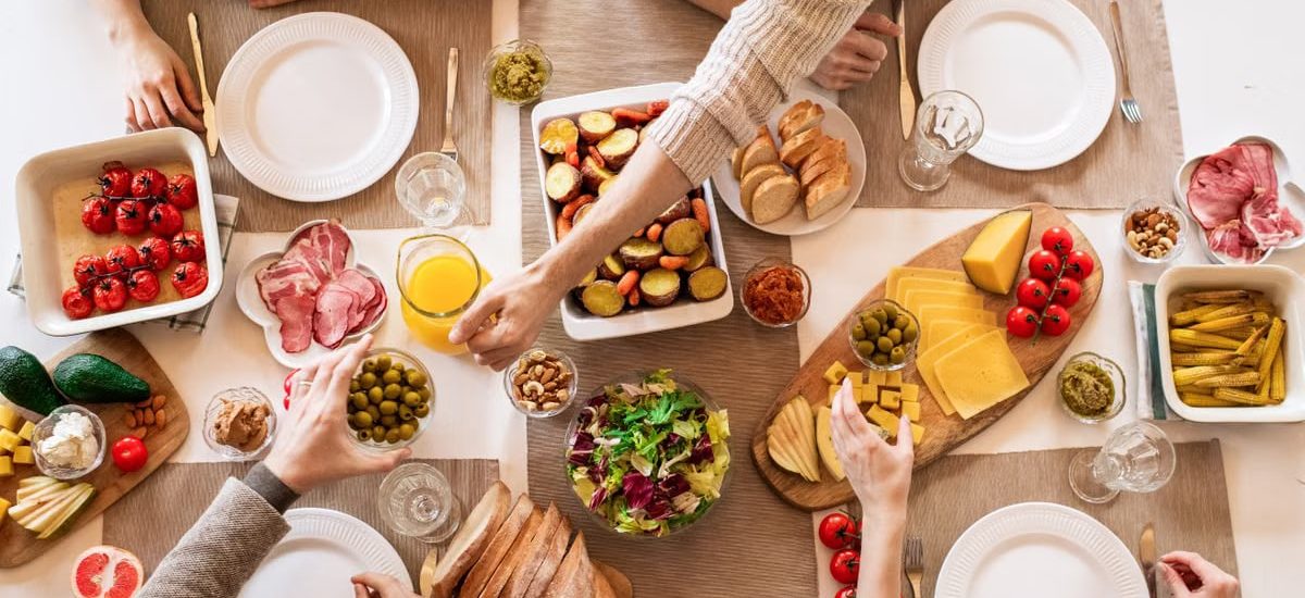 Overhead view of a diverse cheese platter setup for a delicious meal, featuring fresh produce and juices on a table.